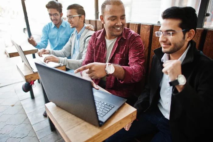 Group of Indian male computing students sitting together and working on their laptops in class